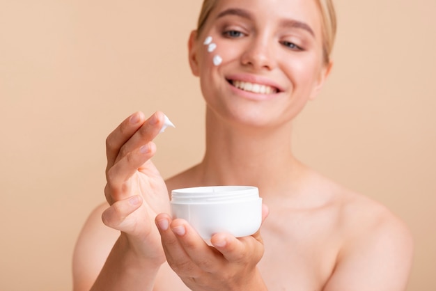 Close-up blonde woman with face cream and jar