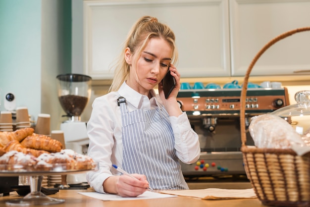 Foto gratuita primo piano di giovane proprietario di negozio biondo del forno che prende ordine del telefono