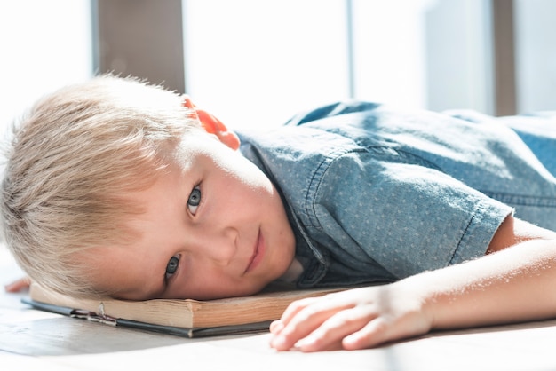 Primo piano della testa pendente del giovane ragazzo biondo su un libro aperto