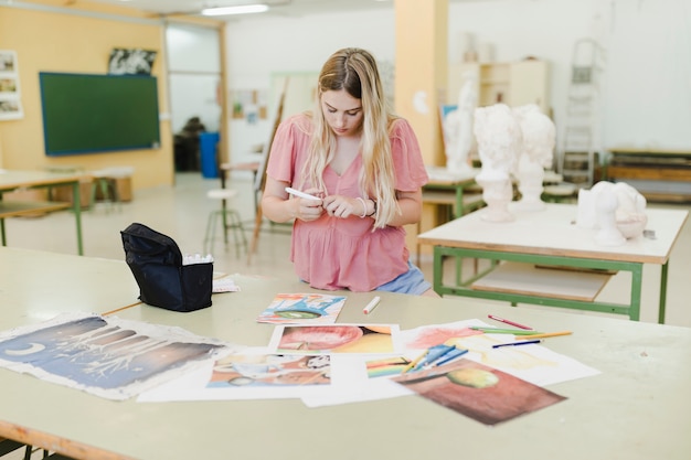 Free photo close-up of blonde young woman doing paintings in paper on table