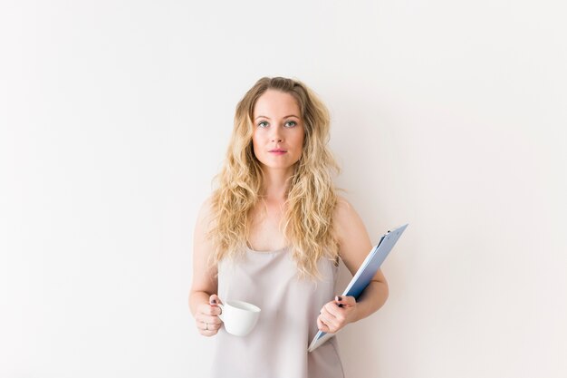 Close-up of blonde young woman holding coffee cup and clipboard