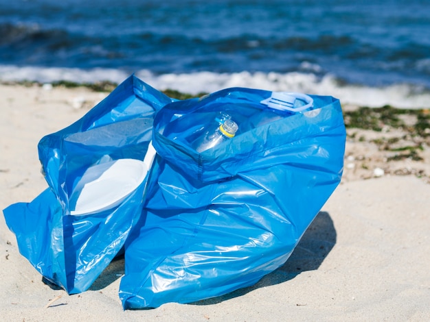 Primo piano del sacchetto di immondizia blu sulla sabbia alla spiaggia