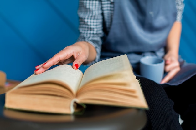 Foto gratuita primo piano della tazza della tenuta della donna e del libro