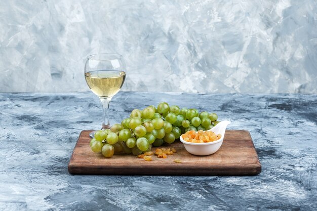 Close-up bowl of grapes, raisins on cutting board with glass of whisky on dark and light blue marble background. horizontal