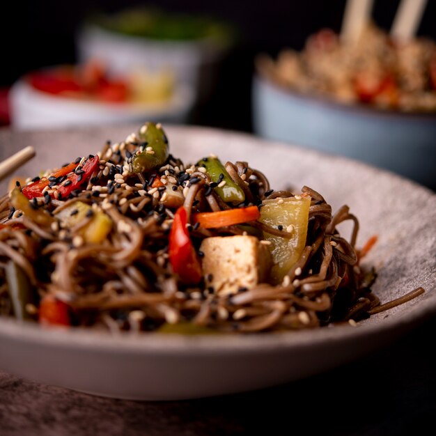 Close-up of bowl of noodles with sesame seeds and vegetables