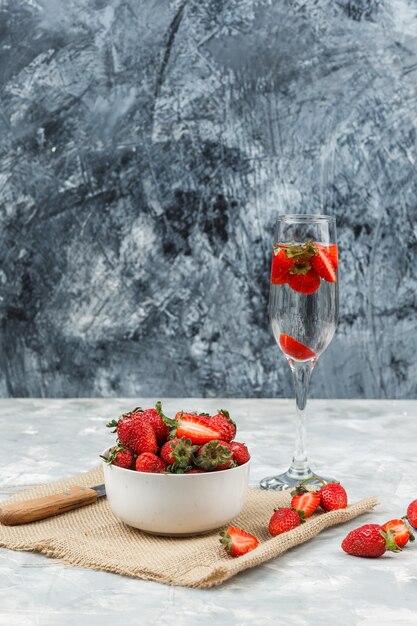 Close-up a bowl of strawberries on a piece of sack with a glass of drink on white and dark blue marble surface. vertical