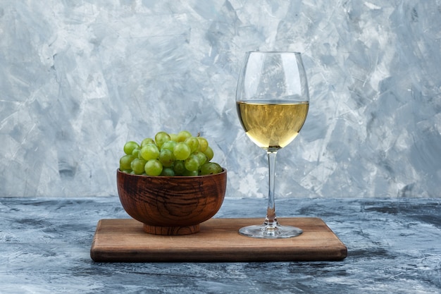 Free photo close-up bowl of white grapes, glass of whisky on cutting board on dark and light blue marble background. horizontal