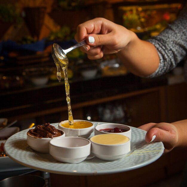 Крупным планом миски со сладкими соусами медом, джемом, шоколадной пастой, сгущенным молоком на белой тарелке