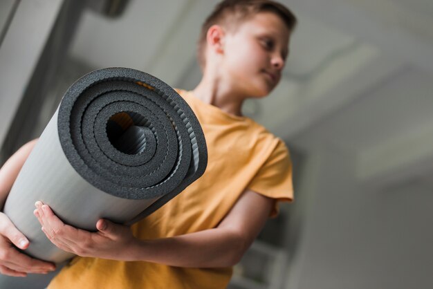 Close-up of a boy holding rolling grey exercise mat looking away