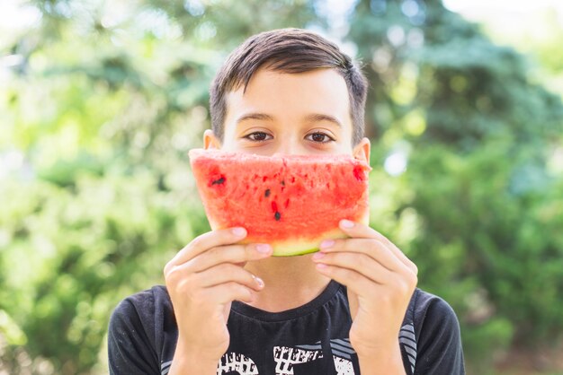 Close-up of a boy holding watermelon slice over his mouth