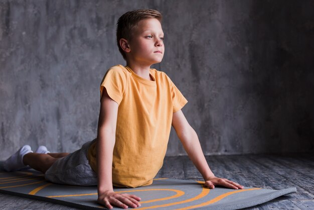 Close-up of a boy stretching on exercise mat in front of concrete wall