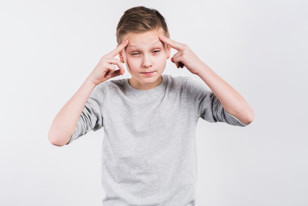 Close-up of a boy suffering from headache against grey background