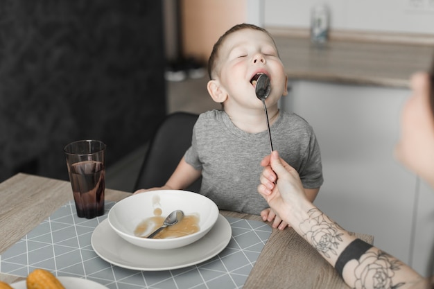 Close-up of a boy with closed eyes licking spoon hold by his mother