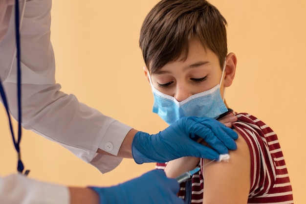 Foto gratuita primo piano ragazzo con maschera che riceve il vaccino