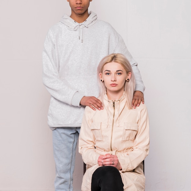 Close-up of boyfriend standing with his blonde young woman sitting on chair against white background