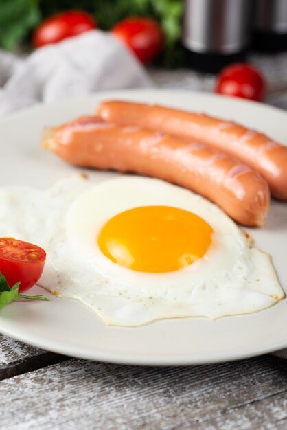 Close-up of breakfast egg and sausages on plate with tomatoes