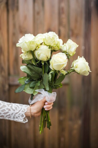 Close-up of bride's hand holding bouquet of roses against wooden backdrop