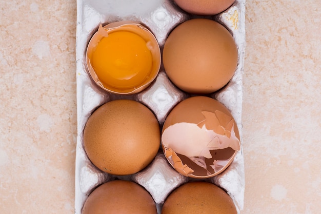 Close-up of broken eggs in white carton on texture backdrop