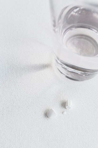 Close-up of broken white pill with glass of water