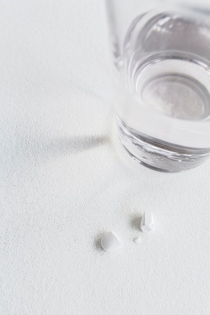 Крупный план сломанной белой таблетки со стаканом воды