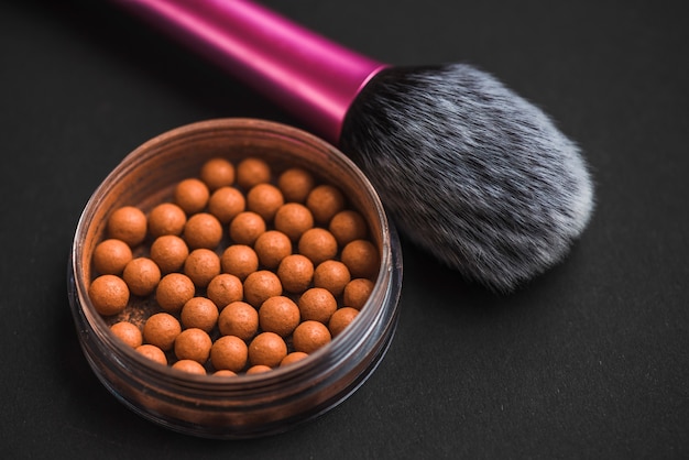 Close-up of bronzing pearls and makeup brush on black surface