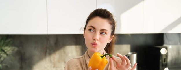 Free photo close up of brunette woman in robe holding yellow pepper thinking what to cook preparing salad or