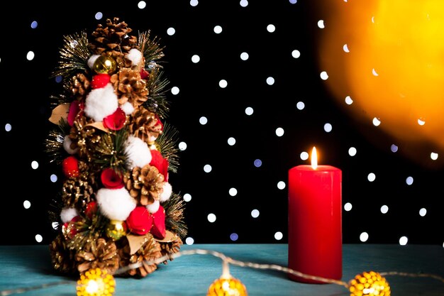 Close up of burning candle next to christmas mini tree on festive bokeh light. Decoration and holiday. Seasonal and new year