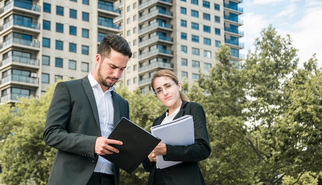 Close-up of businessman and businesswoman holding documents standing in front of building