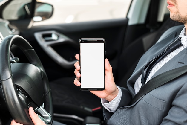 흰색 디스플레이 화면으로 휴대 전화를 보여주는 차를 운전하는 사업가의 근접