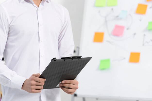 Close-up of a businessman holding black clipboard in hand standing near the flipchart