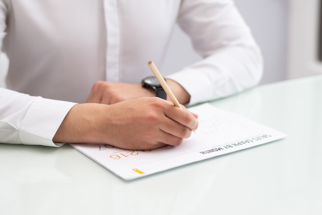 Close-up of businessman sitting at table and writing on paper