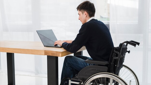 Крупный бизнесмен сидит на инвалидной коляске, используя ноутбук в офисе