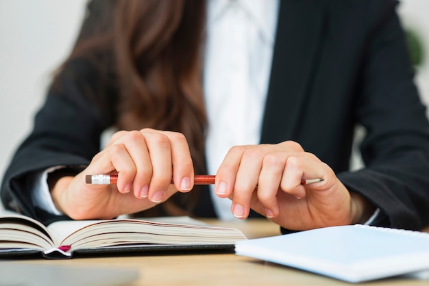 Close-up of a businesswoman holding red pencil in her two hands over the desk