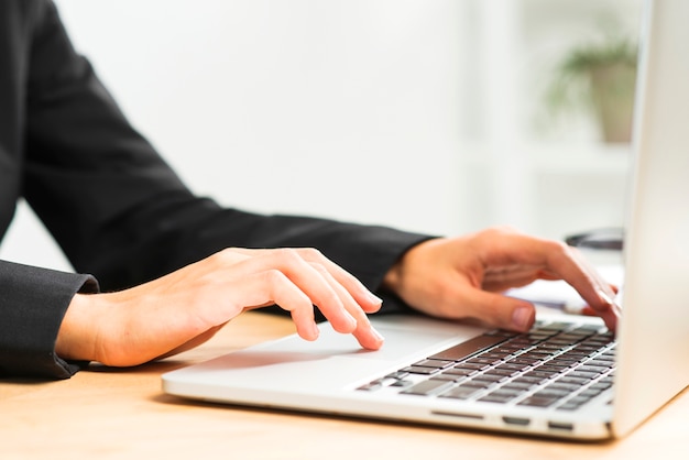 Close-up of businesswoman's hand typing on laptop over desk