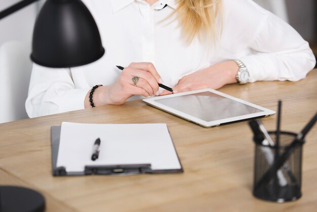 Close-up of businesswoman's hand using digital tablet on wooden over the wooden desk