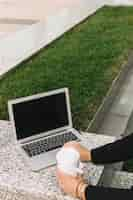 Free photo close-up of a businesswoman's hand using laptop and holding disposal cup