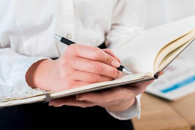 Close-up of businesswoman's hand writing on diary with pen