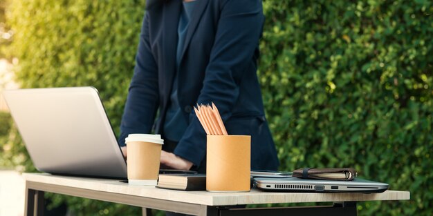 Close-up of businesswoman typing documents on keyboard of laptop hold cup of coffee and business people working at background. selective view. Film effect and sun glare effect
