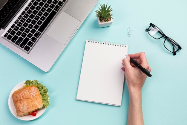 Close-up of businesswoman writing on spiral notepad with pen on office desk