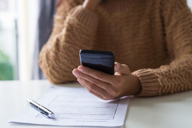 ドキュメントを記入し、電話でsmsをチェックする忙しい女性のクローズアップ