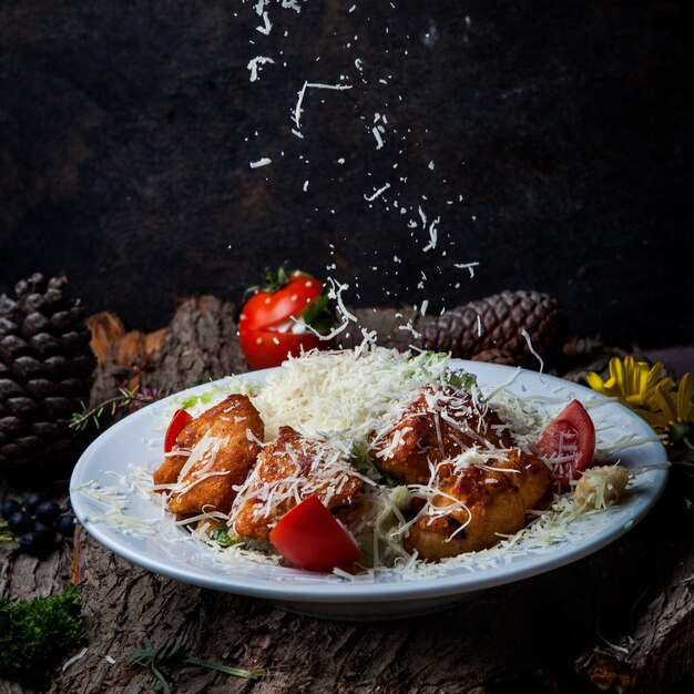 Close-up caesar salad with chicken, tomato, lettuce, olives, crackers, parmesan cheese in a white plate on a dark tree bark