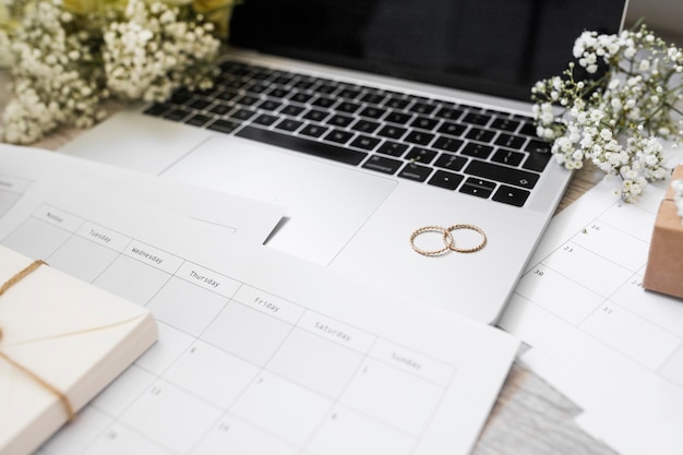 Close-up of calendar; wedding rings; baby's-breath flowers and laptop on desk