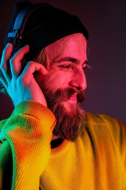 Close up, calm. Caucasian man's portrait on gradient studio background in neon light. Beautiful male model with hipster style in earphones. Concept of human emotions, facial expression, sales, ad.