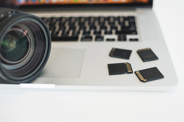 Close-up of camera lens and memory cards on laptop