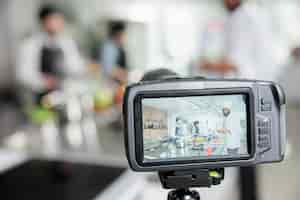 Foto gratuita primo piano della telecamera che registra i lavoratori dell'industria alimentare che cucinano deliziosi piatti gourmet vegetali nella cucina del ristorante. esperti di gastronomia che trasmettono il processo di preparazione dei pasti per il programma di spettacoli culinari tv.