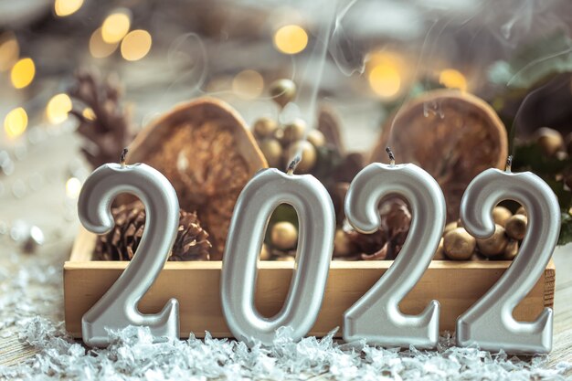 Close-up of candles in the shape of the numbers 2022 on blurred background with Christmas decor and bokeh.