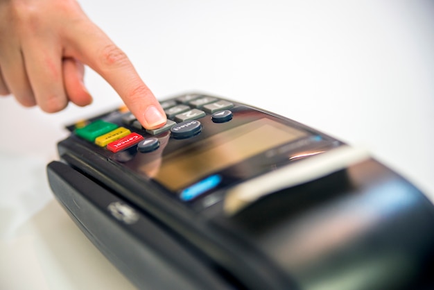 Close-up of cards servicing with POS-terminal, isolated on white background.Female hand with credit card and bank terminal