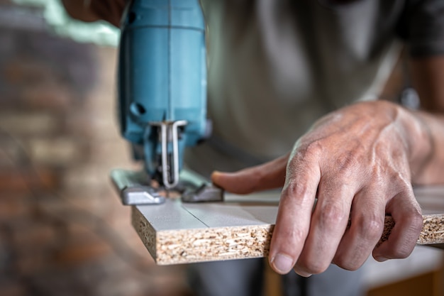 Close-up of a carpenter's hands in the process of cutting wood with a jigsaw.