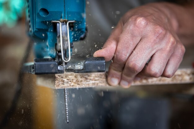 Close-up of a carpenter's hands in the process of cutting wood with a jigsaw.