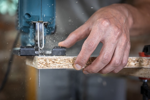 Close-up of a carpenter's hands in the process of cutting wood with a jigsaw.